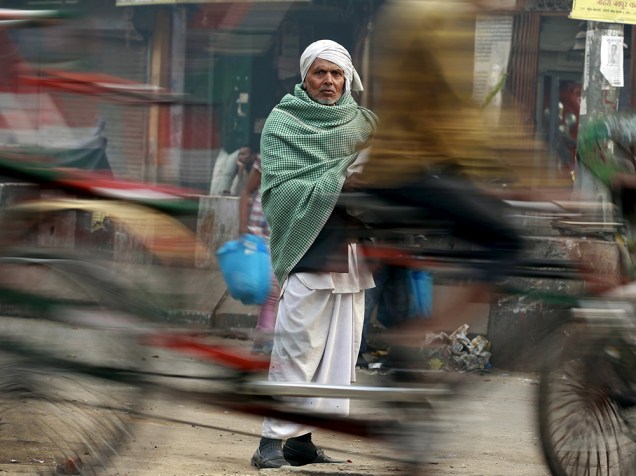 Riquixá passa em frente a um homem em mercado movimentado de Déli, na Índia