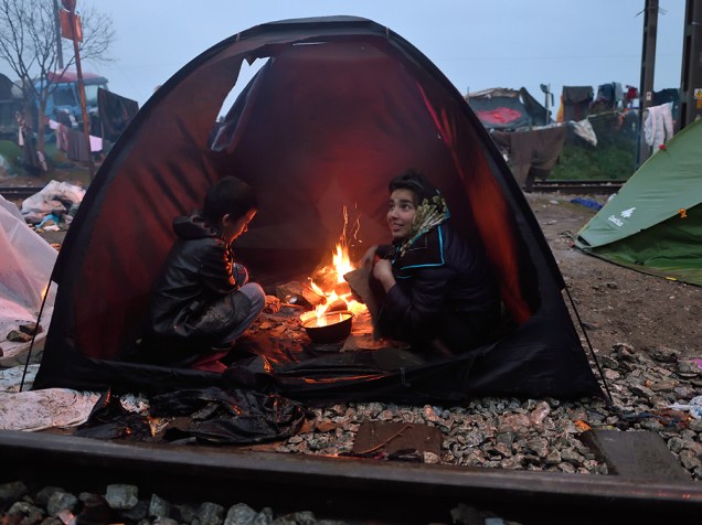 Crianças se sentam ao redor de uma fogueira dentro de uma barraca em um acampamento improvisado na fronteira da Grécia com a Macedônia. Milhares de refugiados e migrantes estão presos no local pelo bloqueio das fronteiras dos Balcãs