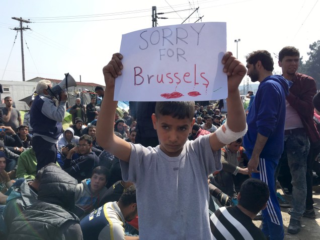 Menino refugiado segura um cartaz com a frase "Desculpe por Bruxelas", durante manifestação contra o fechamento da fronteira greco-macedônia perto da aldeia de Idomeni, na Grécia