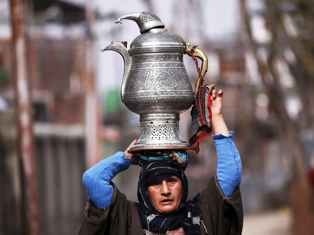 Uma mulher da Caxemira transporta um bule tradicional chamado de samovar na cabeça em uma estrada em Srinagar, nesta quarta-feira (23)