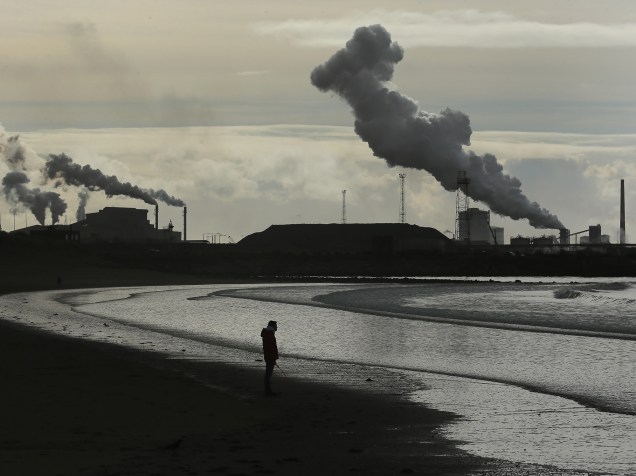 Homem caminha na praia de Aberavon, atrás de uma indústria de metais em Port Talbot, Wales, na Grã-Bretanha - 30/03/2016