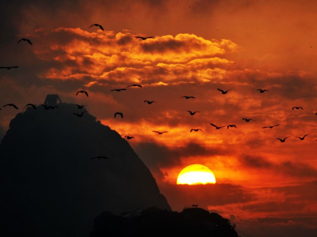 Pássaros Biguás sobrevoam o Pão de Açúcar, vistos de Botafogo, Zona Sul do Rio de Janeiro (RJ), no amanhecer desta sexta-feira (01)