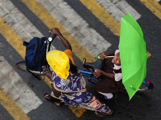 Menina segura um guarda-chuva enquanto atravessar uma estrada na carona de uma bicicleta durante a chuva em Chennai, na Índia - 08/06/2016