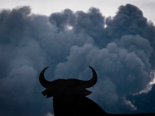 Silhueta de um outdoor em forma de touro é vista entre as nuvens negras de fumaça produzidas pela queima de pneus em um lixão nos arredores de uma zona residencial na cidade de Seseña, na Espanha - 13/05/2016