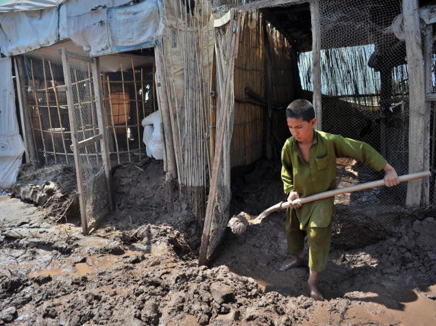 Menino remove a lama da loja onde trabalha após as fortes chuvas e inundações na periferia de Peshawar, no Paquistão - 05/04/2016