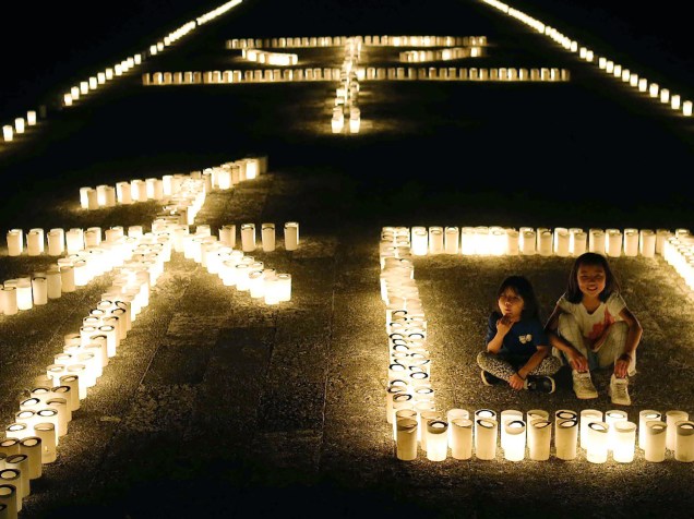 Garotas sentam ao lado de velas dispostas no formato do símbolo chinês que significa "paz". A celebração comemora os 71 anos desde o fim da Guerra de Okinawa, na China - 23/06/2016