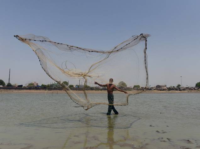 Homem joga sua rede de pesca nas águas rasas do rio Chandola, na Índia, país que esfrenta grave crise de abastecimento de água - 20/05/2016