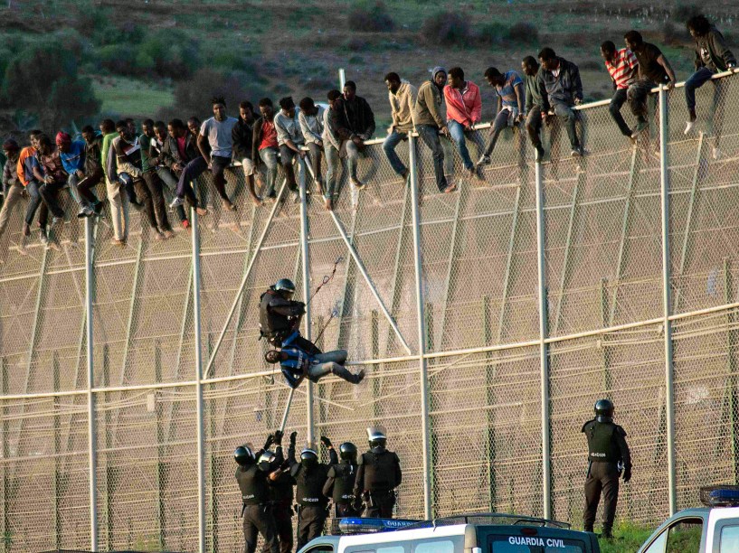 Um guarda civil espanhol leva um imigrante para baixo, enquanto outros se penduram em cerca na fronteira entre Melilla (Espanha) e Marrocos para tentar entrar no território espanhol, no norte da África