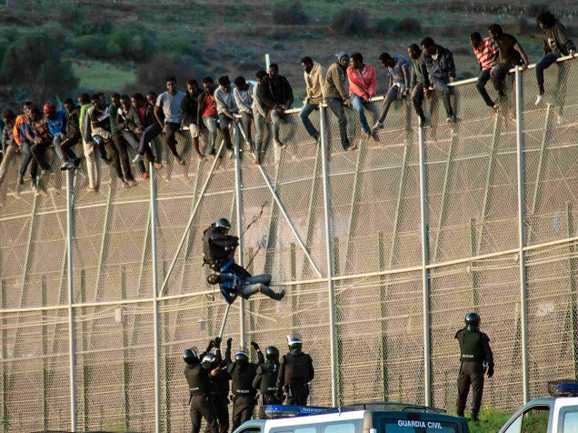 Um guarda civil espanhol leva um imigrante para baixo, enquanto outros se penduram em cerca na fronteira entre Melilla (Espanha) e Marrocos para tentar entrar no território espanhol, no norte da África