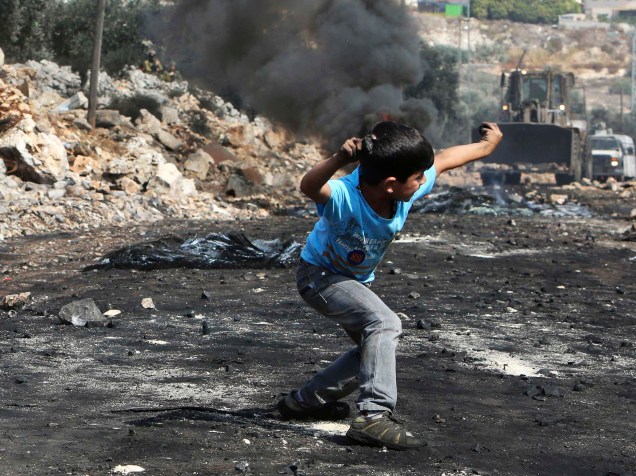 Um menino palestino atira uma pedra nas Forças de Defesa de Israel, durante confrontos após um protesto contra o assentamento de judeus de Qadomem, na aldeia da Cisjordânia