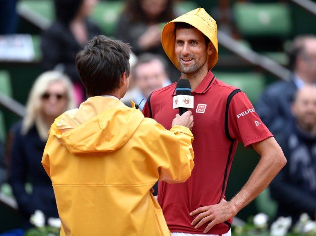 O sérvio Novak Djokovic usa um capuz de capa de chuva enquanto é entrevistado pelo ex-tenista francês Fabrice Santoro após vitória sobre o espanhol Roberto Bautista, em Roland Garros - 01/06/2016