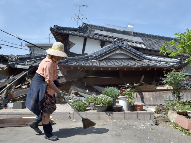 Mulher limpa a frente de sua casa que desabou após terremoto que atingiu a cidade de Mashiki, prefeitura de Kumamoto, no Japão - 15/04/2016