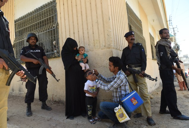 Paquistanesa é escoltada por policiais, enquanto agente de saúde aplica vacina em criança, em Karachi - 21/04/2016