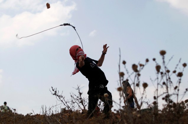 Manifestante palestino usa um estilingue para arremessar pedras em tropas israelenses durante confronto, em Nabi Saleh, na Cisjordânia