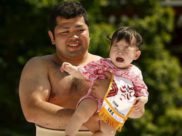 Lutador de sumô amador segura uma criança durante um concurso de choro de bebê em Tóquio; a criança que chorar mais alto e mais forte vence
