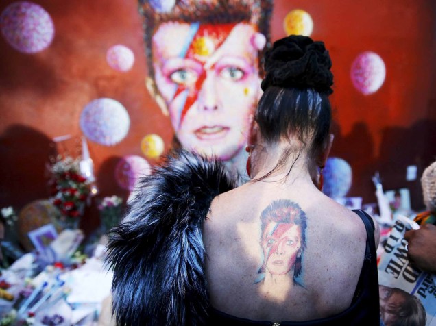 Uma mulher com uma tatuagem de Ziggy Stardust visita um mural de David Bowie no bairro de Brixton, em Londres no dia em que foi anunciada a morte do cantor britânico