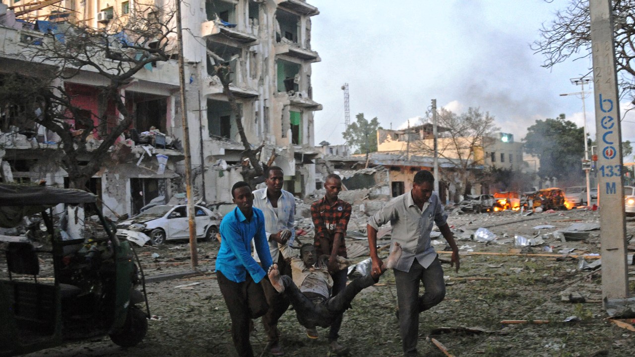 Homem ferido é carregado para fora do Hotel Ambassador, na Somália, depois de um ataque com carro-bomba