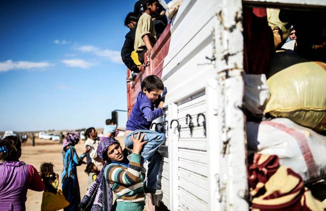 Mãe ajuda seu filho a subir no caminhão que leva sírios aos campos de refugiados na Turquia