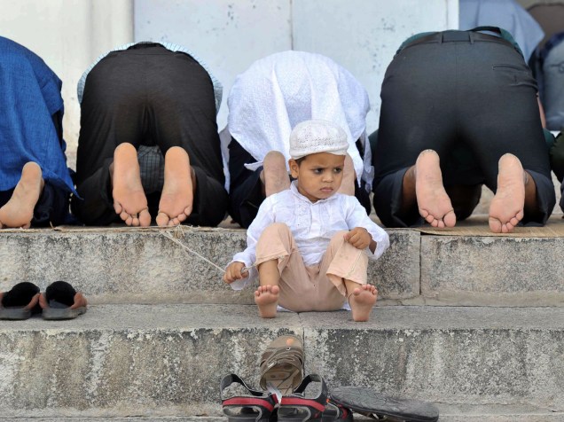 Criança muçulmana sentada em escadaria, enquanto fiéis fazem orações, em Hyderabad, na Índia - 10/06/2016