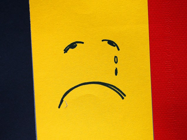 Rosto triste é desenhado em bandeira belga, nesta quarta-feira (23), próximo à estação de metrô Maelbeek, um dos locais que sofreu os atentados em Bruxelas
