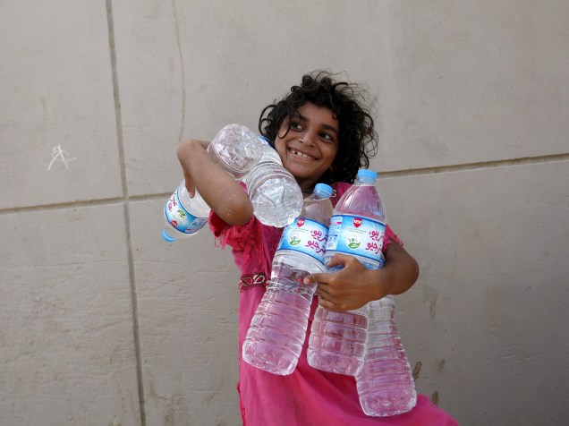 Garota carrega garrafas cheias de água coletadas de uma distribuição de caridade durante uma onda de calor em Carachi, Paquistão, durante o mês do Ramadã