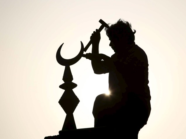 Homem conserta o minarete de uma mesquita com o símbolo de uma lua crescente durante o mês sagrado do Ramadã, em Gidá, Arábia Saudita