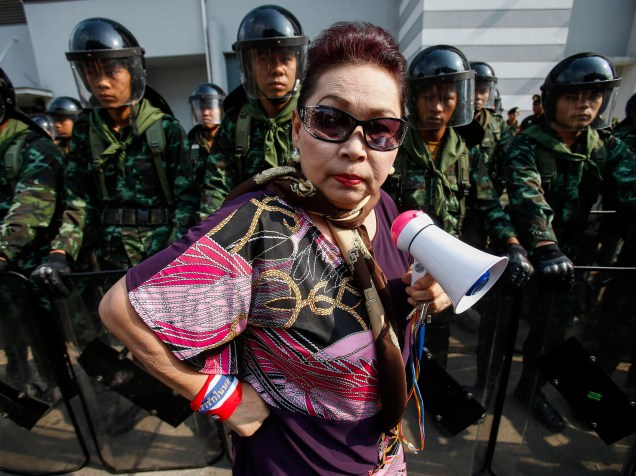 Manifestante contra o governo passa por soldados tailandeses em frente ao Ministério da Defesa. O regime militar assumiu o governo depois de um golpe de Estado, em maio