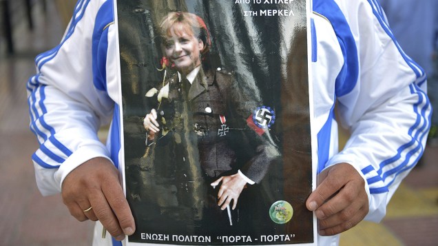 Cartaz de manifestante mostra Angela Merkel vestindo trajes nazistas, em protestos na visita oficial da chanceler alemã à Grécia