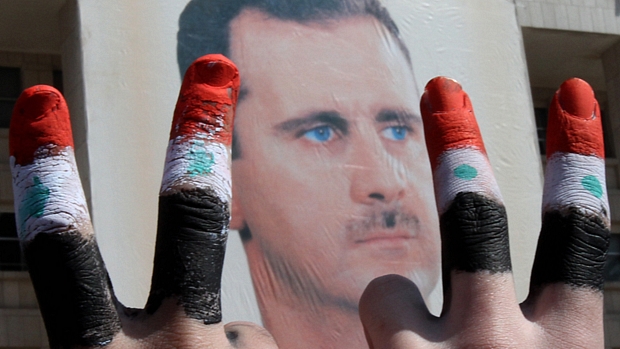 Manifestantes fazem o sinal da paz diante de imagem do presidente Assad