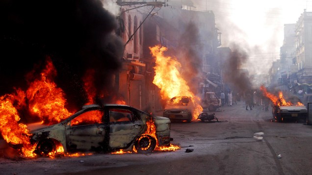 Carros em chamas nas ruas de Karachi, no Paquistão, nesta terça-feira (22). Homens armados abriram fogo durante um comício político na cidade paquistanesa hoje, matando pelo menos nove pessoas e deixando mais de 30 feridos