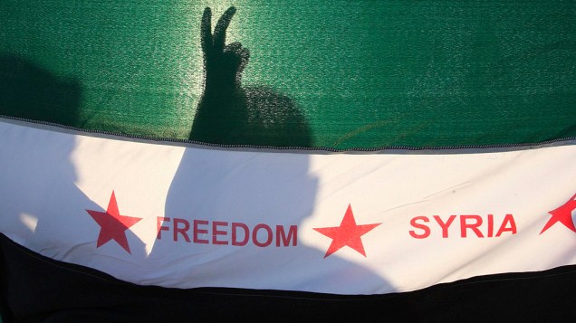 Manifestantes com bandeira da oposição síria durante uma manifestação contra o presidente, Bashar Al-Assad em frente à embaixada da Síria, em Amã