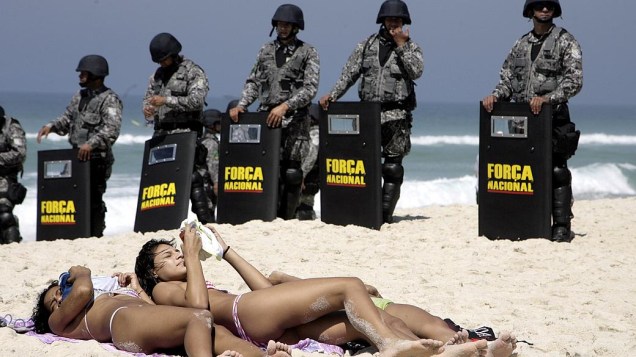 Banhistas aproveitam o dia de sol enquanto homens da Força Nacional isolam àrea na praia da Barra da Tijuca, em dia de protesto contra o leilão do pré-sal
