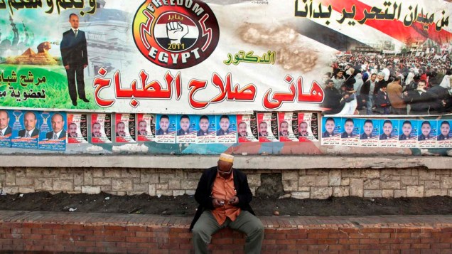 Homem senta embaixo de banner eleitoral do candidato independente, Dr. Hany Salah El Tabakh, que contém a mensagem "Na praça Tahrir começamos e todos nós continuaremos" no Cairo, Egito