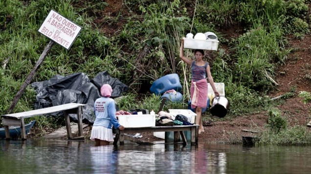 Rosilene Costa Silva (de costas) e Adriele da Silva Balão usam a água do Xingu para lavar roupas ao lado de placa contra Belo Monte. Com as obras, casas serão removidas