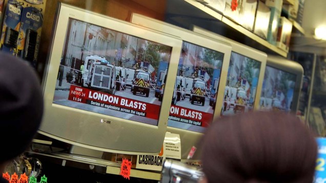 Após as explosões, pessoas assistem ao noticiário através de uma vitrine em Londres
