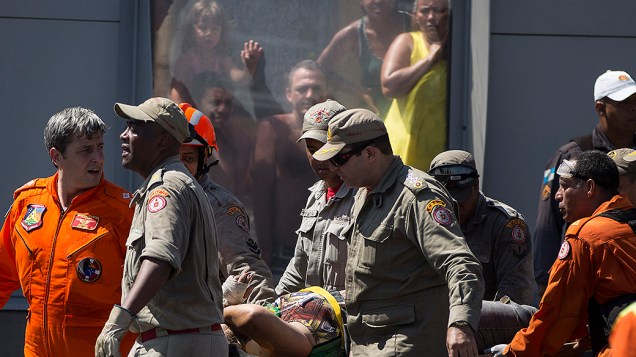 Equipes de resgate carregam uma mulher retirada de seu carro esmagado por uma ponte que desabou após ser derrubada por um caminhão, na Linha Amarela, no Rio de Janeiro