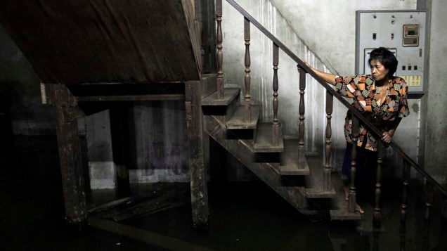 Mulher avalia situação de casa afetada pelas enchentes na Chinatown, em Bangcoc, na Tailândia