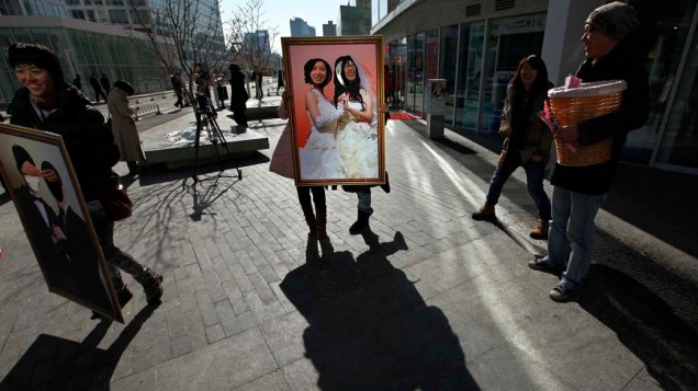 Em Pequim, chinesas posam para fotos com um retrato de casamento de noivas lésbicas durante campanha no Dia dos Namorados