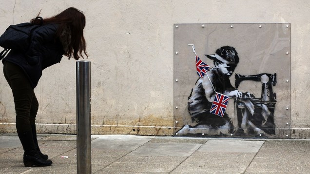 Mulher olha para uma obra do artista Banksy sob uma tampa de plástico em Londres, Inglaterra