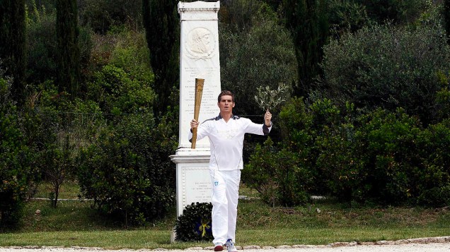Spyridon Gianniotis, grego campeão mundial de natação com a tocha e um ramo de oliveira durante cerimônia na cidade antiga de Olímpia, Grécia