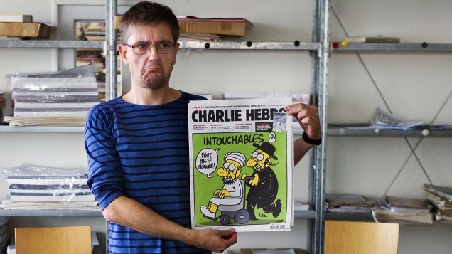 Editor do satírico Charlie Hebdo conhecido apenas como Charb exibe a última edição da revista, que traz na capa uma charge sobre o Islã. A França anunciou que fechará temporariamente embaixadas e escolas em 20 países após a publicação