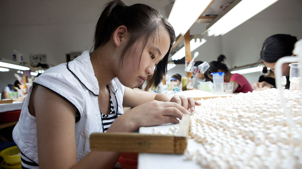 Trabalhadora organiza pérolas de acordo com tamanho e cor, em fábrica chinesa