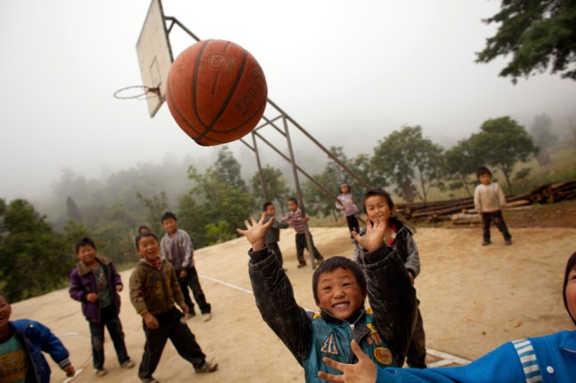Crianças da única escola de Heshan jogam basquete no intervalo das aulas. A maioria é filha de trabalhadores que migraram para as cidades. As que têm mais sorte recebem a visita dos pais uma vez por ano