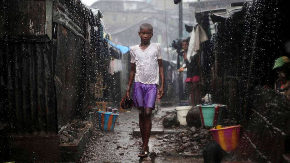 Menino caminha sob forte chuva na favela de Susan Bay, na capital de Serra Leoa