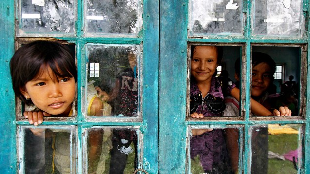 Crianças olham pela janela de uma casa em um campo de refugiados na cidade Bijni, na Índia