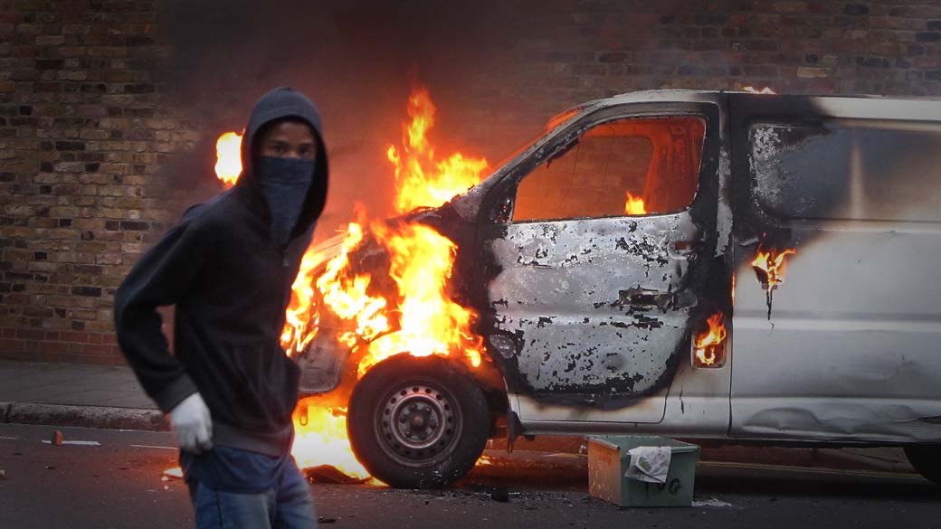 Jovem encapuzado nas proximidades de um veículo queimado no bairro de Hackney, Londres. Tumultos e saques continuam acontecendo em algumas regiões da capital inglesa