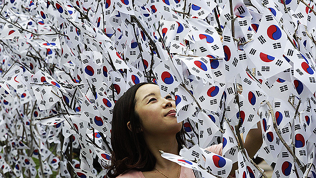 Mulher sul-coreana observa bandeiras do país penduradas em árvores na véspera da comemoração da independência do país