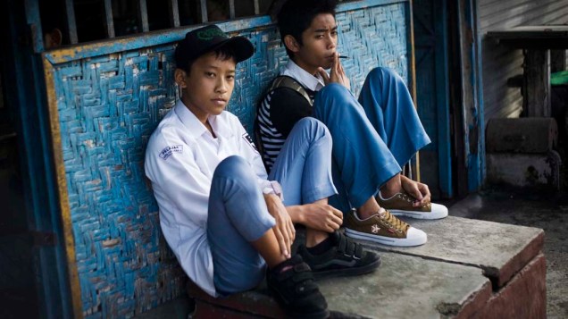 Estudantes fumam antes da escola na cidade de Yogyakarta , Indonésia. A maior parte dos cigarros tem um sabor adocicado, pois o tabaco é misturado ao cravo, uma especiaria considerada parte da história e da cultura da Indonésia. Isso faz com que o início do vício seja mais fácil para os jovens