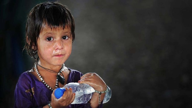 Criança refugiada afegã carrega garrafa de água distribuída em centro da ONU para refugiados nos arredores de Peshawar, Paquistão