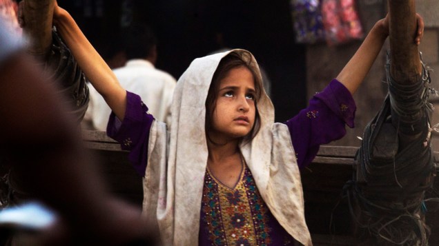 Menina refugiada afegã brinca em frente a porta de sua casa numa favela de Islamabad, Paquistão